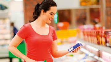 Mulher no supermercado lendo rótulos de alimentos - Dreamstime