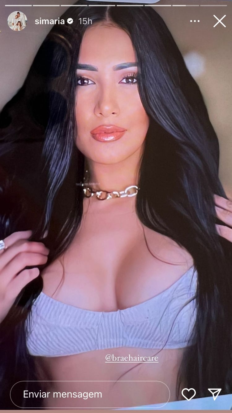 A cantora Simaria com um top curto lilás, uma corrente tipo choker dourada e os cabelos pretos soltandos, olhando diretamente para a câmera
