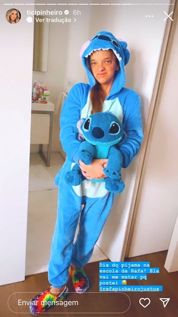 Foto de Rafa Justus usando um pijama do personagem Stitch, da Disney, e segurando um boneco de pelúcia do mesmo personaem. Na foto, está escrito em azul: "“Dia do pijama na escola da Rafa! Ela vai me matar porque postei”