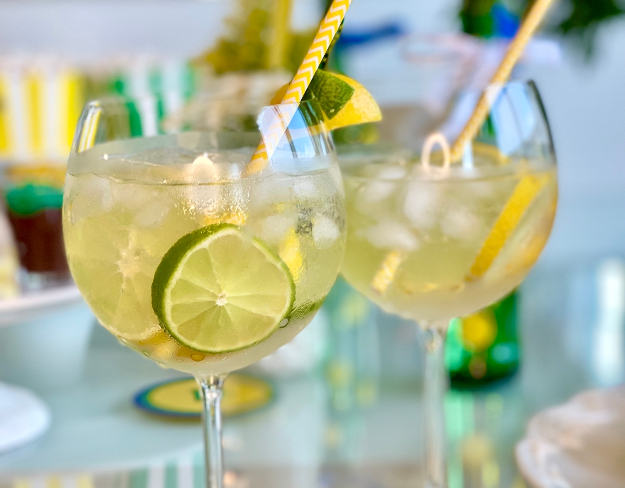 Duas taças de gin com bebida e rodelas de limão taiti e siciliano dentro, além de um canudo listrado em amarelo e branco