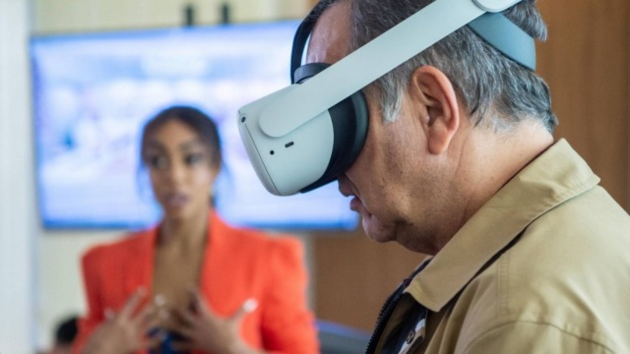 Em 'Travessia', Guerra (Humberto Martins) com um óculos de realidade virtual e Talita (Dandara Mariana) apresentando um projeto no fundo
