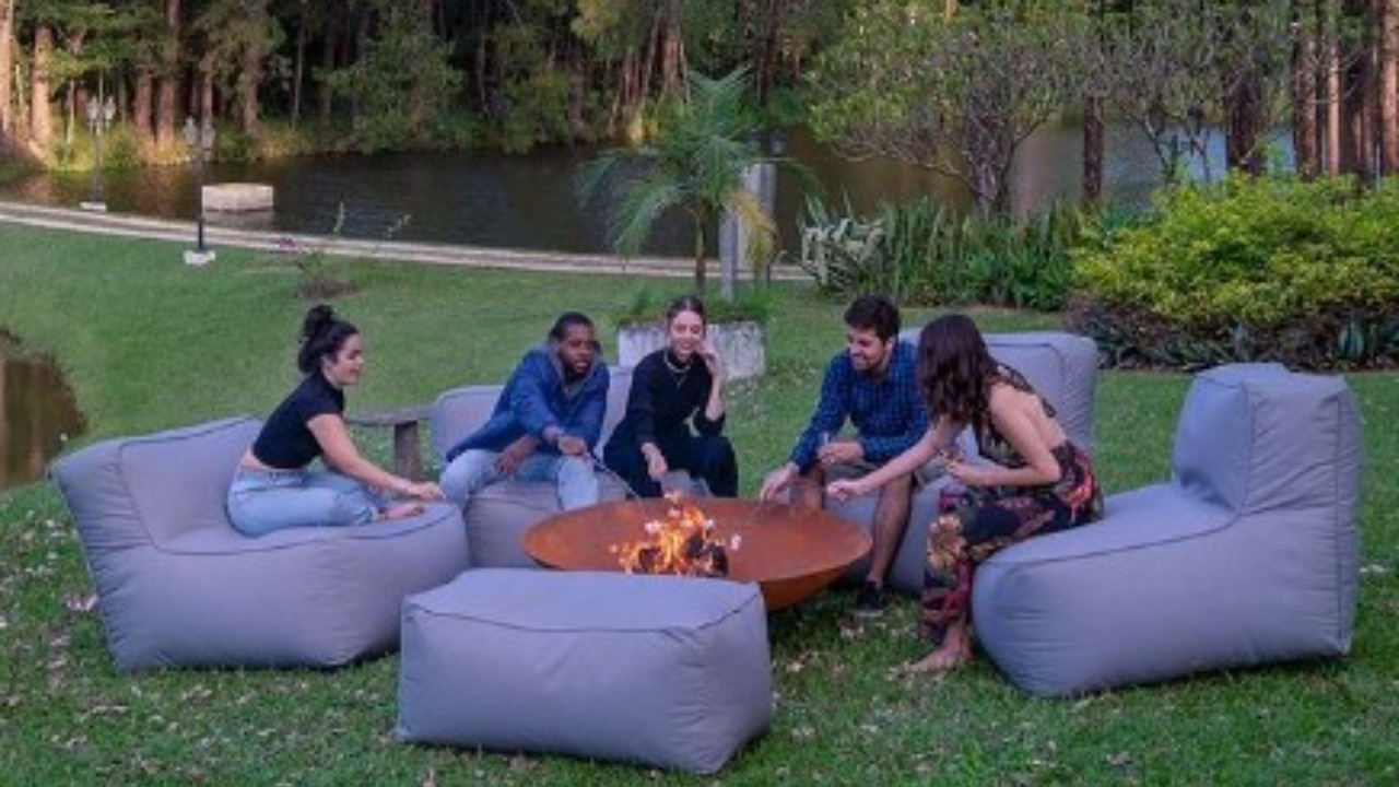 Amigos sentados nos pufes em um jardim ao redor de uma fogueira